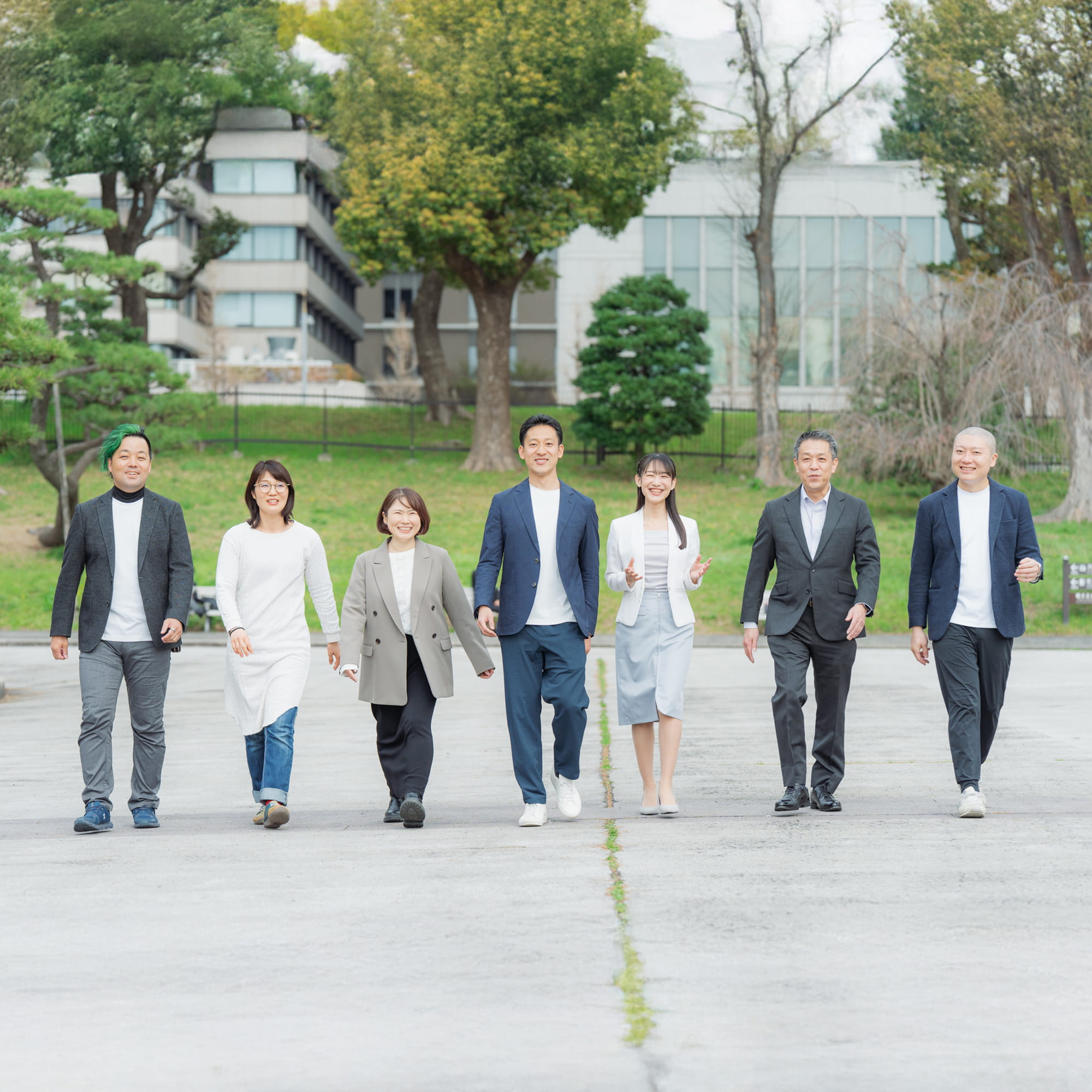屋外の広場で7名のチームメンバーが横並びに笑顔で歩くチーム集合写真