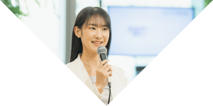 白いジャケットを着た女性がマイクを持ち、前を向いてスピーチしている様子